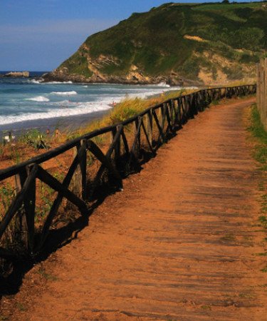 Paseo rústico cerca de Zarautz con una valla de madera, rodeado de naturaleza y vistas al mar.